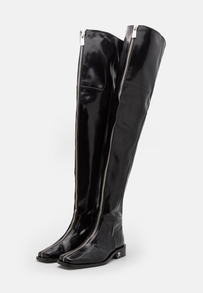 Svarta, blanka, stövlar över knäna med en stilren design. Har silverfärgade dragkedjor framtill och en fyrkantig tå. Låg klack.
