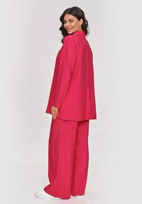 Fuksjowy dwuczęściowy zestaw składający się z luźnej kurteczki z długim rękawem i szerokich spodni, wykonany z gładkiego materiału o minimalistycznym designie.