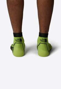 Calcetines verdes hasta el tobillo con acentos negros. Incluyen puños acanalados y detalles del logo en la parte trasera. Tejido suave y ajuste ceñido.