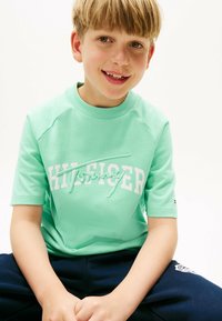 T-shirt a maniche corte verde menta con logo "Tommy Hilfiger" in bianco ricamato in rilievo, abbinato a pantaloni blu navy. Tessuto di cotone morbido.