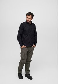 Black long-sleeve shirt with two chest pockets, paired with olive cargo pants featuring multiple pockets and a tapered fit. Black footwear completes the outfit.