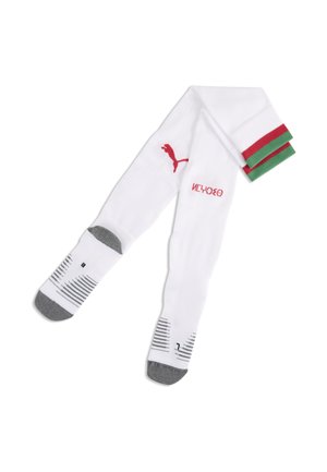 Calze sportive bianche con punte e talloni grigi, logo Puma rosso, marchi neri sulle pianta dei piedi e risvolti a righe verdi e rosse piegati su uno sfondo bianco.