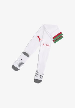 Calze sportive bianche con punte e talloni grigi, logo Puma rosso, marchi neri sulle pianta dei piedi e risvolti a righe verdi e rosse piegati su uno sfondo bianco.