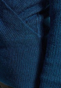 Dettaglio di un tessuto in maglia blu che mostra modelli testurizzati e a coste in un materiale spesso e morbido.