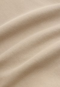 Bež tkanina glatke teksture i suptilne rastezljivosti, prikazujući mekani, ujednačeni uzorak pletenja i nježni pad.