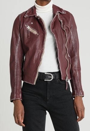 Person iført en vinrød læderbikerjakke over en hvid rullekrave og sorte jeans med et sort bælte med sølvspænde.