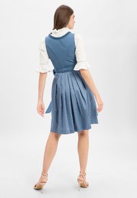Blue sleeveless dress with a pleated skirt and patterned fabric. Features a ruffled white blouse with lace trim and a tied waist.