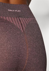 Lila träningsleggings med en texturerad yta, som har en bred midja märkt med "ONLY PLAY" och ett grafiskt mönster nära höfterna.