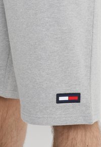 Jasnoszare szorty na osobie z małą prostokątną naszywką w kolorze czerwonym, białym i niebieskim blisko dolnego brzegu.