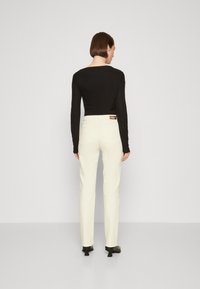 Top negro de manga larga combinado con pantalones blancos ajustados con un bolsillo trasero y una cinturilla de marca, complementado con zapatos de tacón negros.