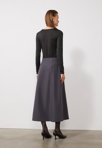 Un haut noir à manches longues associé à une jupe grise longue jusqu'au sol, présentant une texture lisse et un design épuré. Des talons noirs complètent le look.