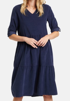 Navy blue, knee-length dress in soft fabric with a v-neck, three-quarter sleeves, and tiered skirt with gathered detail. Buttons on sleeves.