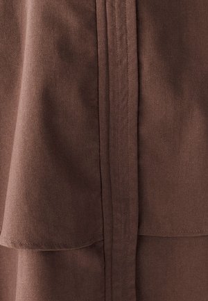 Brūns audums ar gludu tekstūru, ar slāņu dizainu un tīrām šuvēm gar malām un šuvēm. Nav redzamu rakstu vai akcentu.