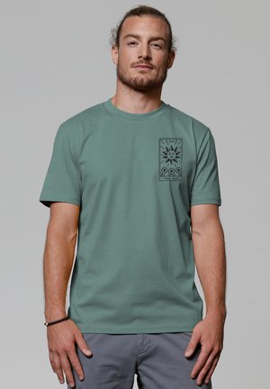 T-shirt en coton vert à manches courtes. L'avant présente un graphique noir d'un soleil et du texte dans un design de carte. Col rond et coupe décontractée.