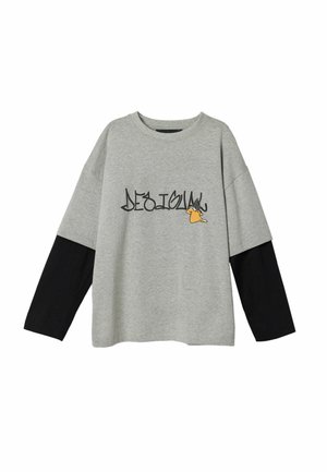 Grå oversize t-shirt med sorte lange ærmer, med stiliseret "DESIGUAL" tekst og en tegneserieaccent på forsiden. Materiale af bomuldsblanding.