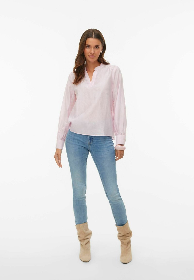 Lys rosa bluse med lange ermer, v-hals og mansjetter, kombinert med lyseblå skinny jeans og beige løstsittende støvler.