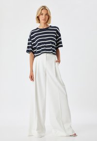 Camiseta recortada a rayas en azul marino y blanco con mangas cortas, combinada con pantalones de pierna ancha blancos de talle alto, que presentan líneas limpias y una textura suave.