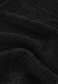 Close-up van zwarte, gestructureerde stof met een zacht, verhoogd, lusvormig oppervlak en lichte plooien die schaduwen en diepte creëren.