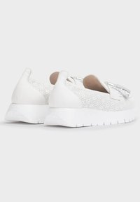 Zapatos blancos de tipo slip-on con piel perforada, detalles texturizados y una suela de goma blanca gruesa. Forma redondeada con un diseño de perfil bajo.