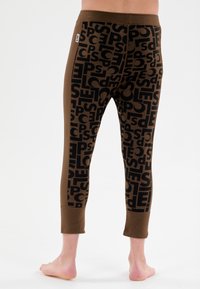 Braune Leggings mit einem schwarz wiederholenden Textmuster. Entworfen mit einem figurbetonten Schnitt und verkürzter Länge, ausgestattet mit einem festen Bund und Knöchelabschlüssen.