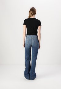 Black fitted t-shirt paired with high-waisted, flared blue jeans featuring two back pockets, denim texture, and a slight wash effect.