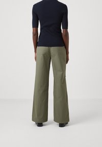 Široké kalhoty olivově zelené barvy z lehké látky s hladkou strukturou a dvěma zadními kapsami, doplněné tmavým žebrovaným topem.