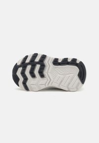 Suola di scarpa sportiva in bianco e nero con un motivo a zigzag, sezioni testurizzate e aree rialzate per la presa e la stabilità.