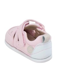 Zapato de niña pequeña en color rosa, con parte superior de tela, tira de velcro, suela blanca y punta redonda. Presenta un pequeño logo circular en el lado y un interior suave.