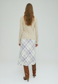 Beige gebreide trui met een gestructureerd patroon gecombineerd met een geruite midirok in wit, paars en bruin, aangevuld met bruine laarzen met hoge hakken.