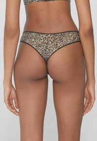 String en léopard avec bord noir, en matériau maille semi-transparente et design taille basse, vu de l'arrière.