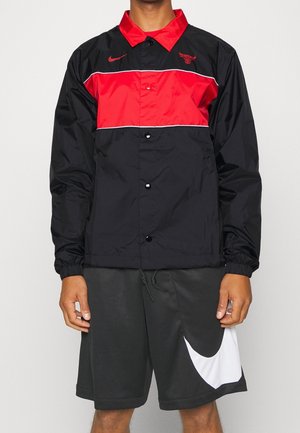 Man draagt een zwarte en rode Chicago Bulls Nike windbreaker en zwarte Nike shorts met een grote witte swoosh op het linkerbeen.