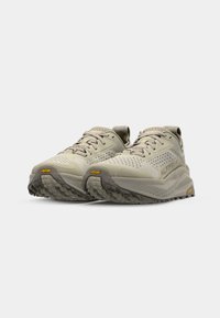 Baskets de course beiges avec un uppers texturé, des détails perforés et une semelle extérieure robuste, arborant la marque Vibram et une semelle intermédiaire rembourrée.