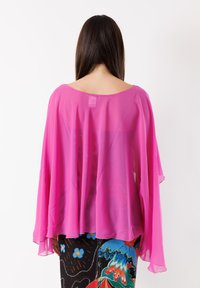Blusa rosa trasparente con ampio scollo e maniche volant, caratterizzata da una vestibilità larga che scivola. Abbinata a pantaloni multicolore con motivo.