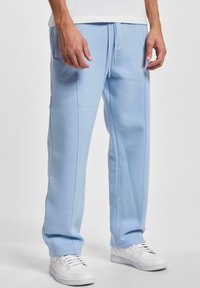 Lichtblauwe sweatpants van zachte stof, met een relaxte pasvorm, een trekkoord middenband en contrasterende zijstiksels. Gemaakt in combinatie met witte sneakers.