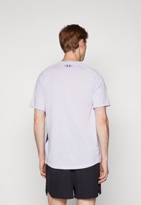 Camiseta deportiva de color púrpura claro con mangas cortas, que presenta un escote redondo y acentos púrpuras en los lados. Material suave y que absorbe la humedad.