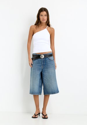 Witte ribbed top met één schouder, gecombineerd met blauwe denim culottes en een gestudeerde zwarte riem met een grote zilveren gesp. Zwarte sandalen.