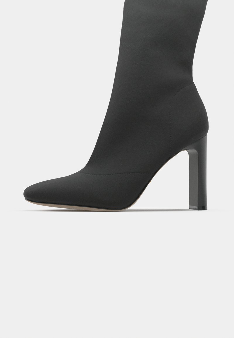 Schwarze Stiletto-Stiefelette mit einem eleganten, sockenähnlichen Design, spitzem Zeh, glattem Stoff und einem quadratischen hohen Absatz. Minimalistische Ästhetik.