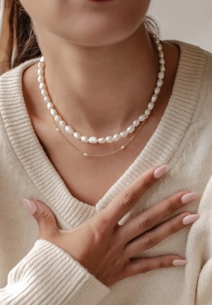 Two layered necklaces featuring white pearls, one strung on a gold chain. A knitted cream sweater is visible in the foreground.