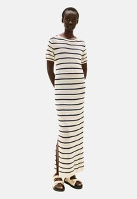 Szydełkowa sukienka w kremowym kolorze z granatowymi pasiakami, z okrągłym dekoltem, krótkimi rękawami i bocznymi rozcięciami dla większej swobody ruchów.