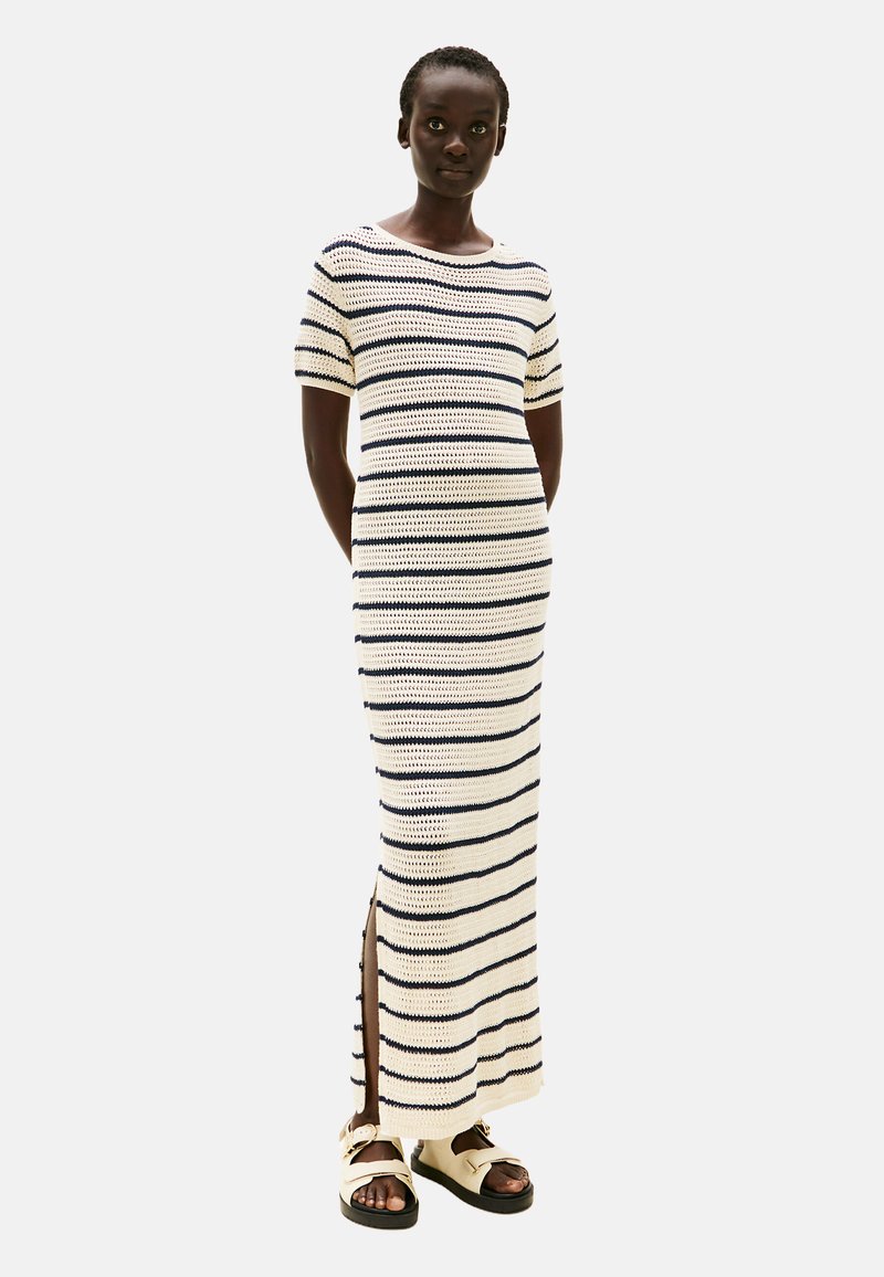 Szydełkowa sukienka w kremowym kolorze z granatowymi pasiakami, z okrągłym dekoltem, krótkimi rękawami i bocznymi rozcięciami dla większej swobody ruchów.