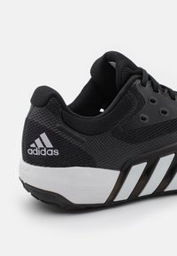 Svart Adidas träningsskor med vit sula och tre vita ränder, med nättyg och vadderad ankelkrage.