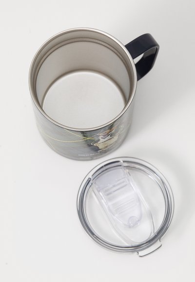 Pahar de călătorie din oțel inoxidabil cu mâner închis la culoare și capac din plastic transparent detașabil, așezat pe o suprafață albă.