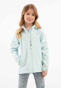Giacca zip-up azzurro chiaro con una texture liscia, tasche laterali e un piccolo logo a forma di ombrello sul petto, abbinata a jeans in denim scoloriti.