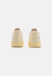 White patent leather sneakers with beige accents, round toe, flat sole, and textured back. Features minimal branding and smooth finish.