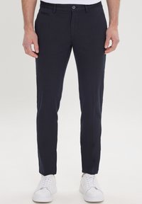 Pantalon bleu marine à coupe slim avec devant plat, fermeture à un bouton et poches latérales. Associé à des baskets blanches.
