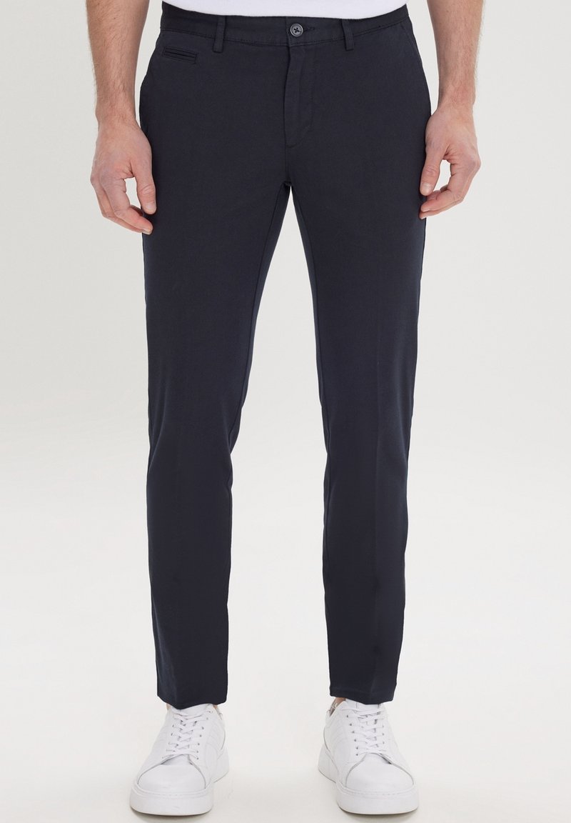 Pantalon bleu marine à coupe slim avec devant plat, fermeture à un bouton et poches latérales. Associé à des baskets blanches.