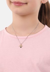Collana con pendente a forma di ape in oro e nero su una catena argentata, indossata sopra una maglietta rosa. Il pendente mostra caratteristiche distintive e accenti in smalto.