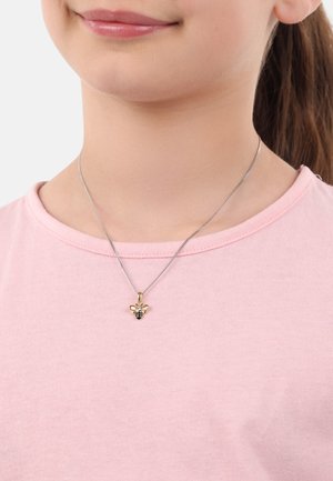 Gold- und schwarze Bienenanhänger-Halskette an einer Silberkette, getragen über einem pinken Shirt. Der Anhänger zeigt ausgeprägte Merkmale und Emaille-Details.