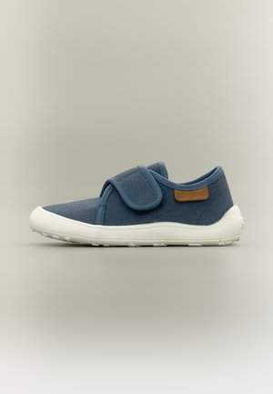Zapato informal de tela azul con suela blanca y una amplia tira de velcro, que presenta un pequeño parche de logo marrón en el lateral.