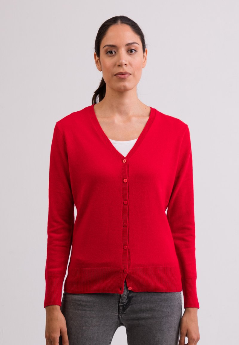 Röd stickad cardigan med v-ringning, långa ärmar och knäppning framtill. Slät textur, ribbat nederkant, bären över en vit topp.